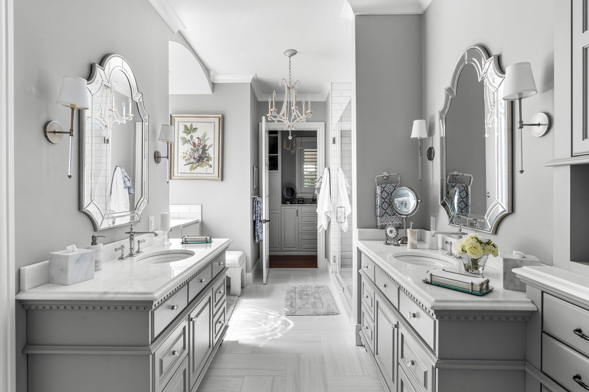 A bright, symmetrical double-vanity bathroom featuring light gray cabinets, marble countertops, and ornate wall mirrors.