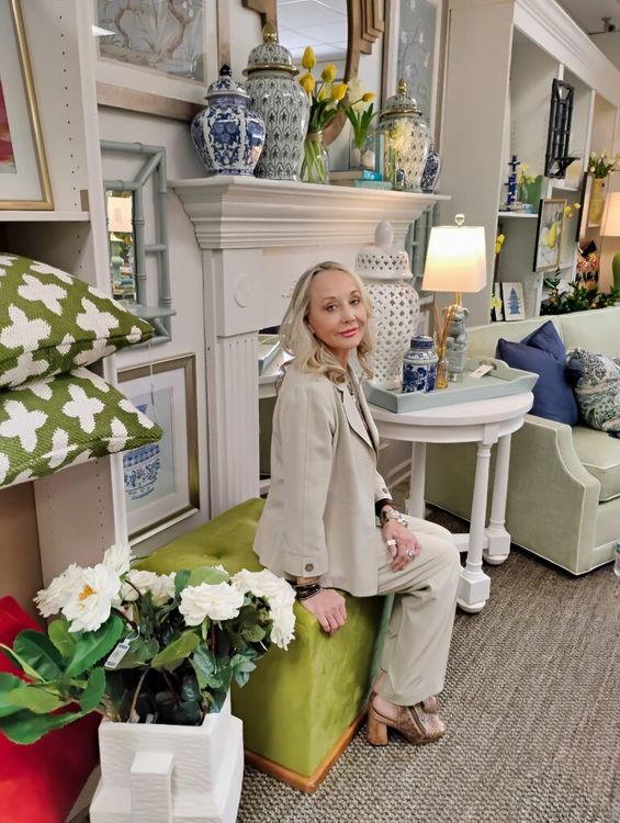 A person sitting on a lime green ottoman in a brightly lit home decor shop surrounded by furniture, pillows, and lamps.