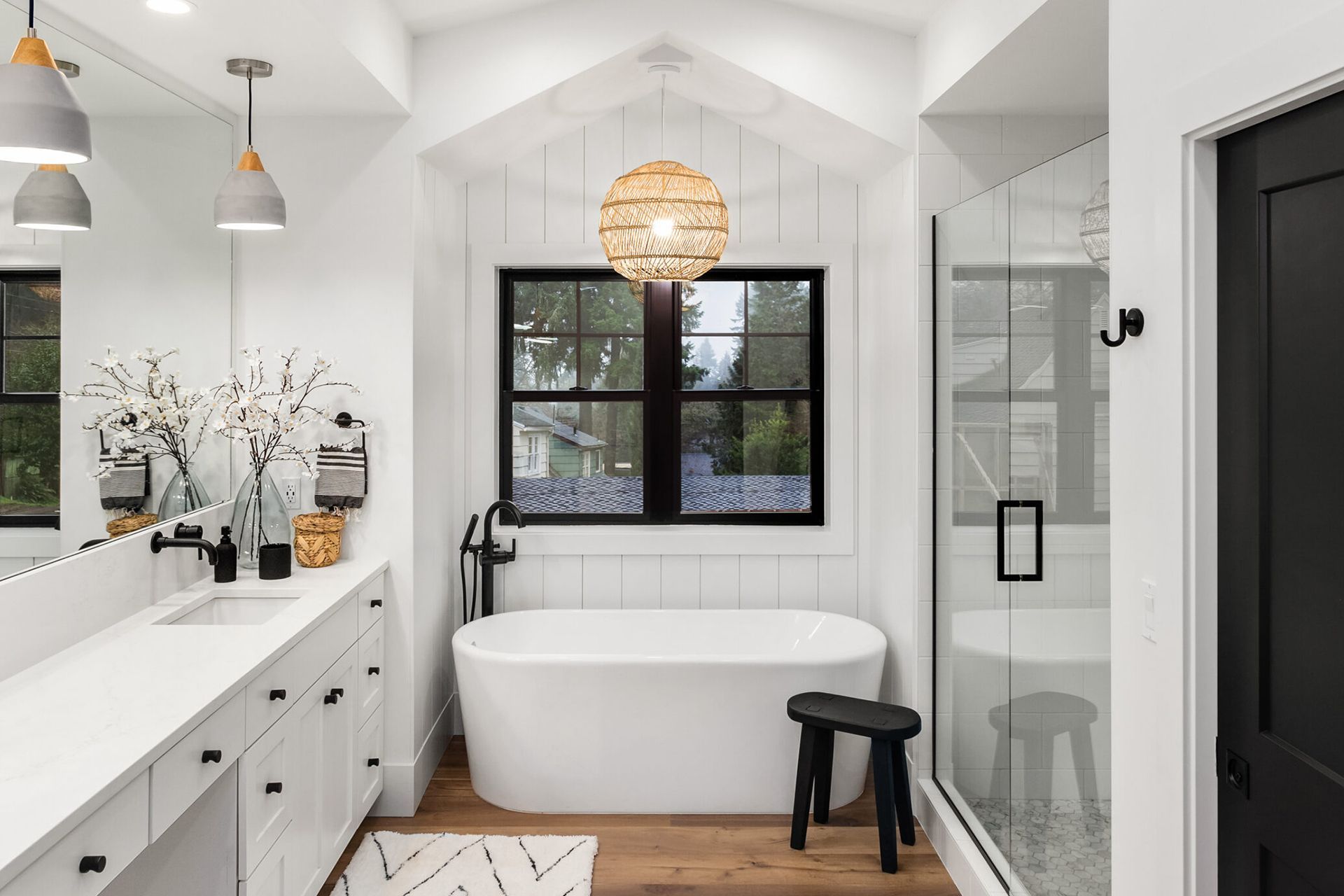 A modern white bathroom with a freestanding tub, black accents, double vanity, and a walk-in glass shower.