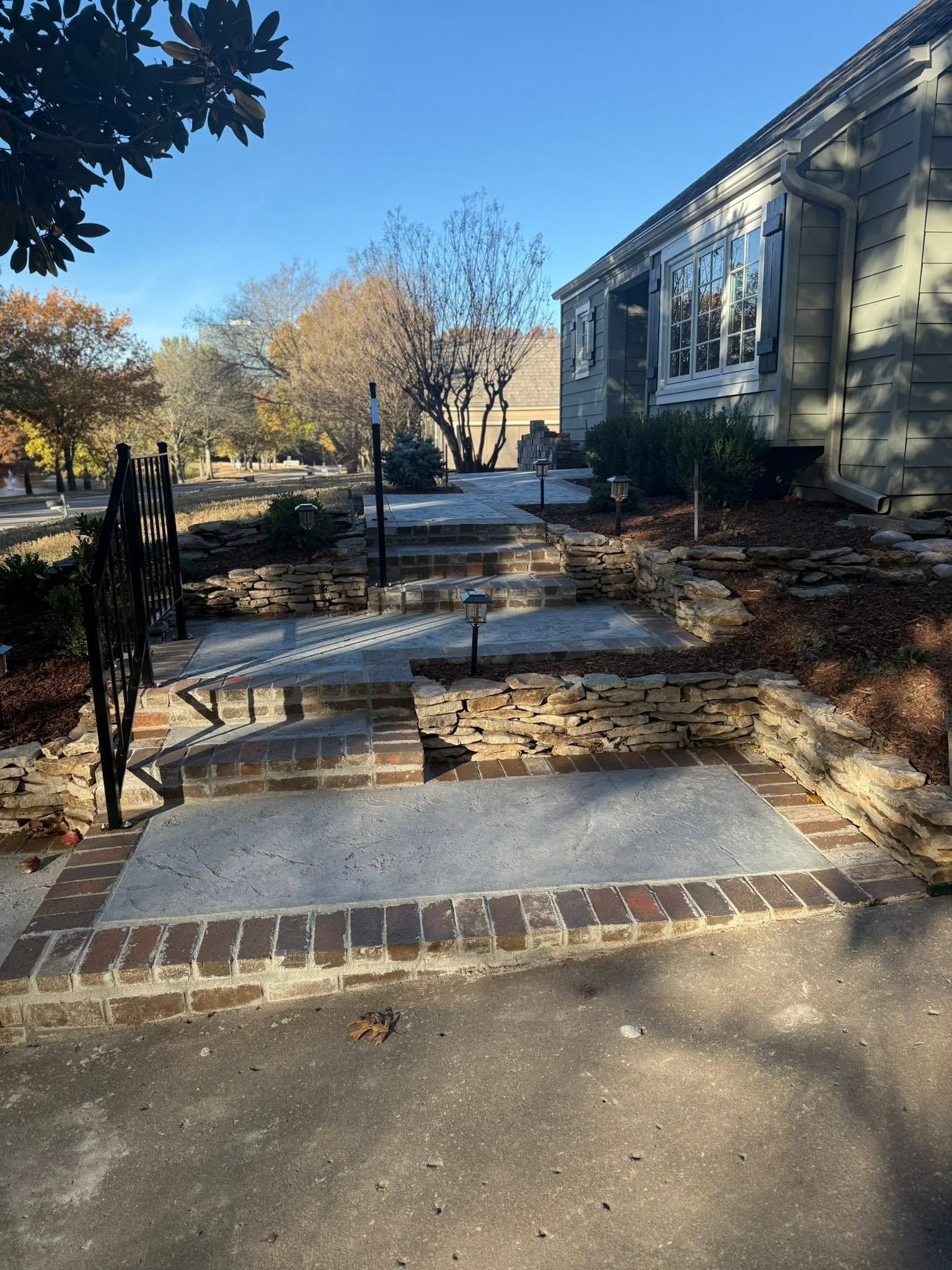 Front walkway with brick steps and a lighted building entrance beside autumn trees and shrubs