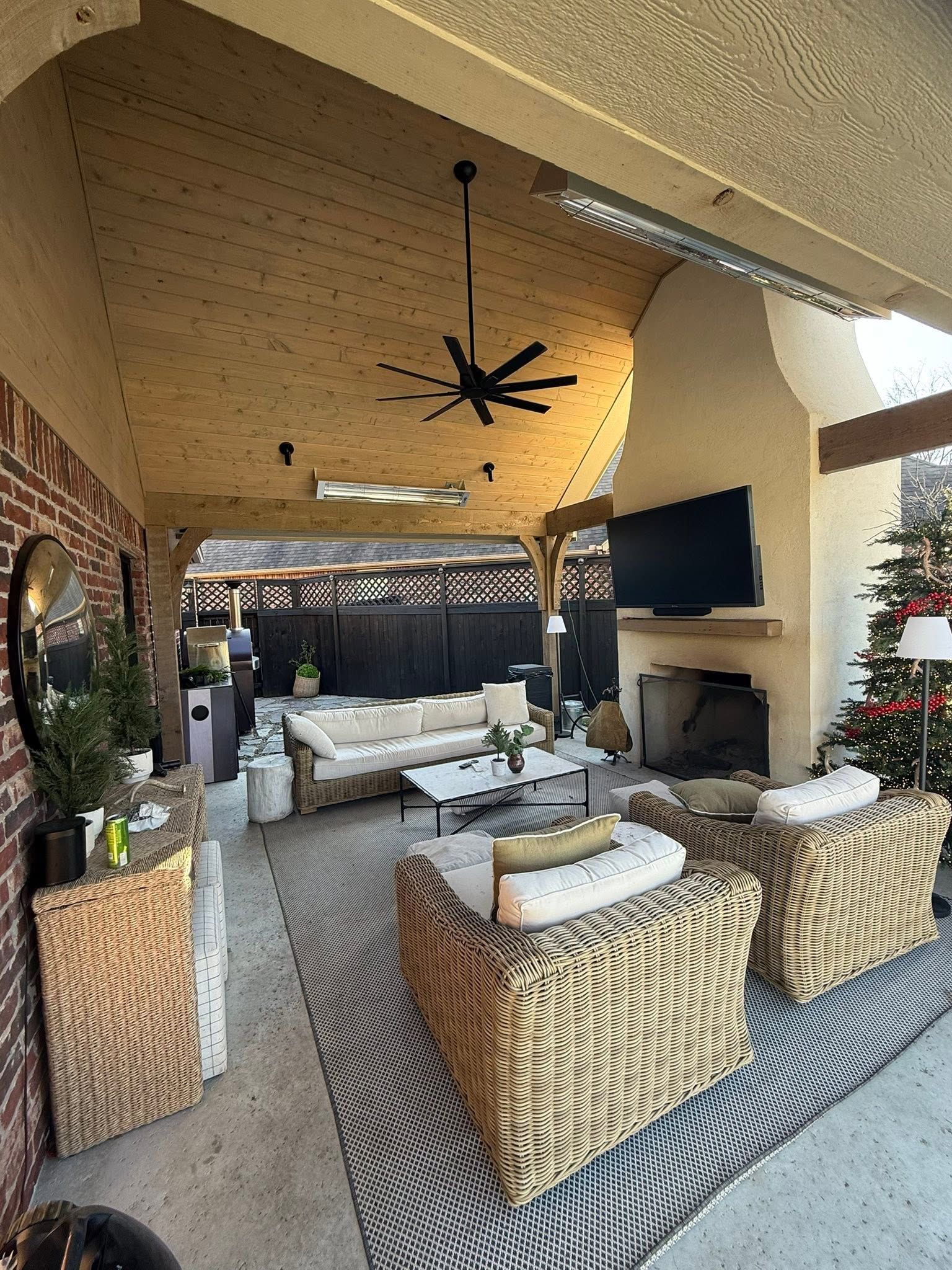 Covered outdoor patio with wicker seating, patterned rug, fireplace, and ceiling fan overlooking a pool area