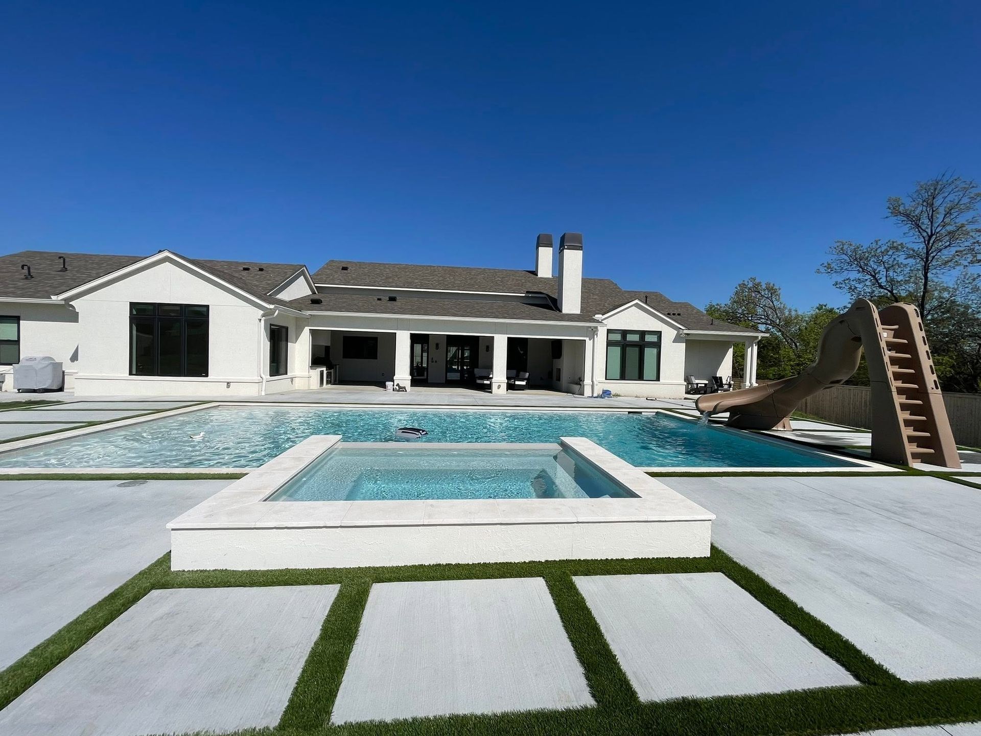 Backyard pool and patio with white house under a clear blue sky