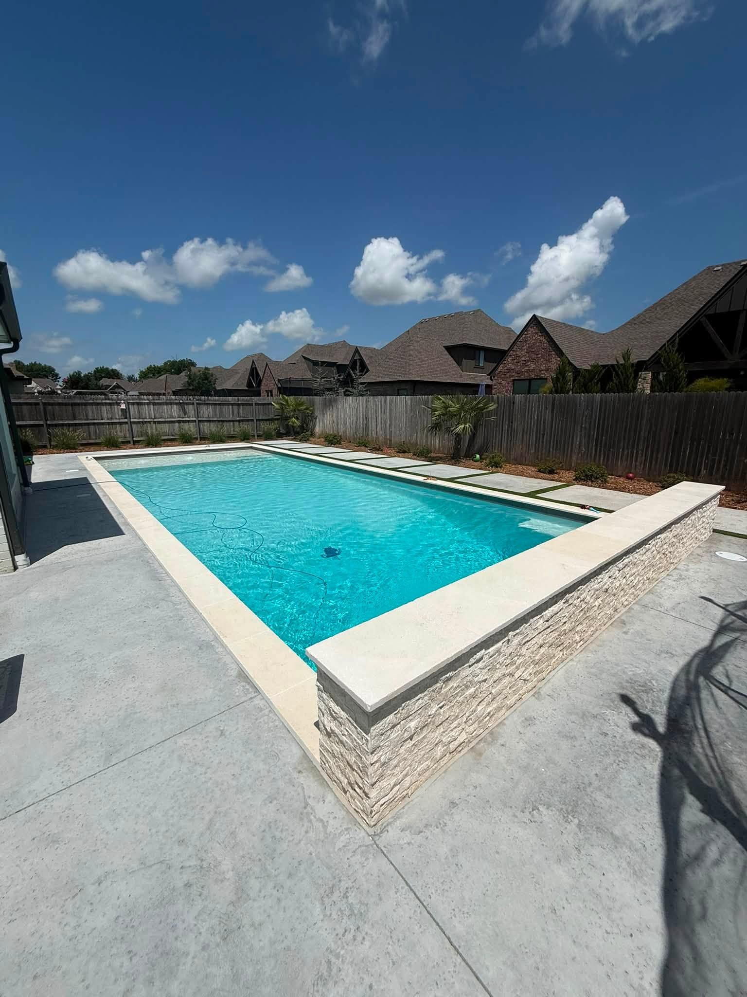 Outdoor swimming pool with turquoise water beside a paved patio and thatched-roof buildings under a blue sky