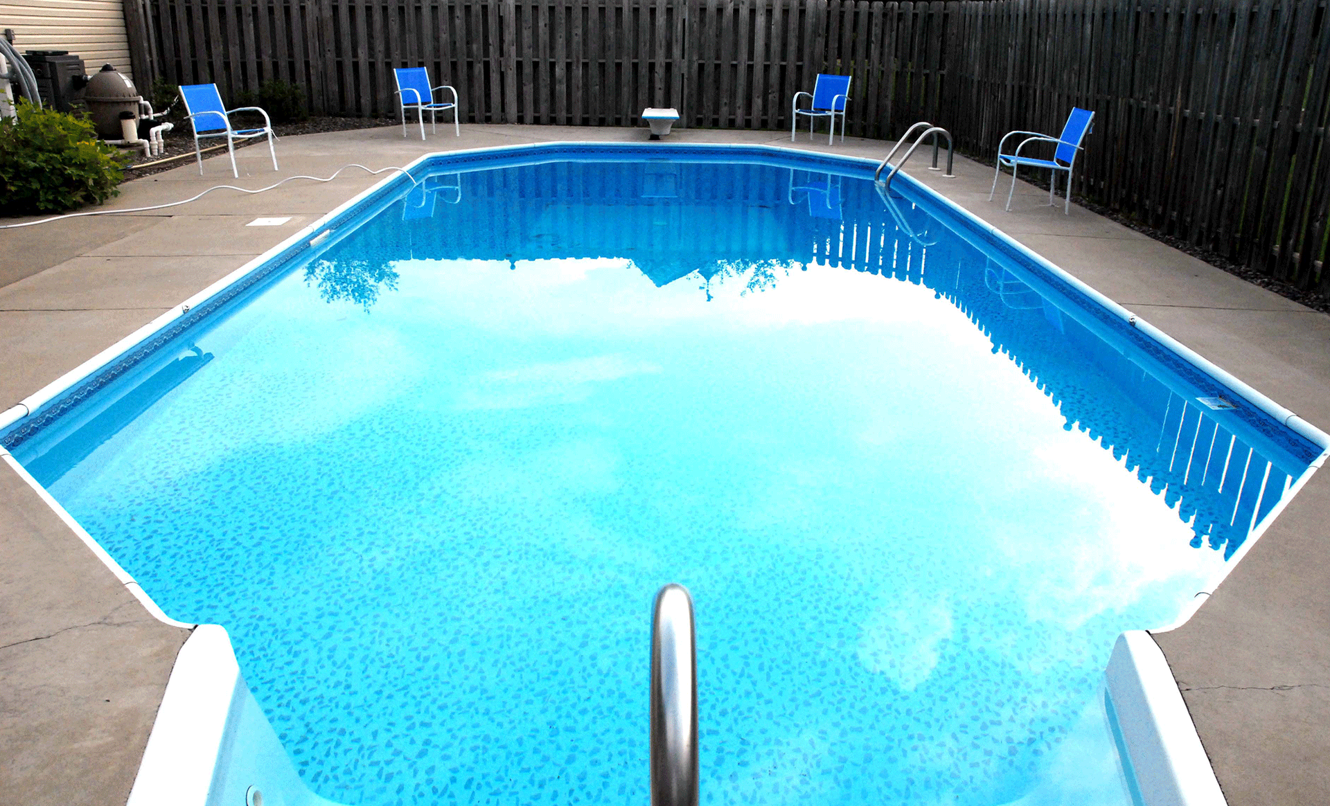 Backyard swimming pool with bright blue water and chairs along the deck
