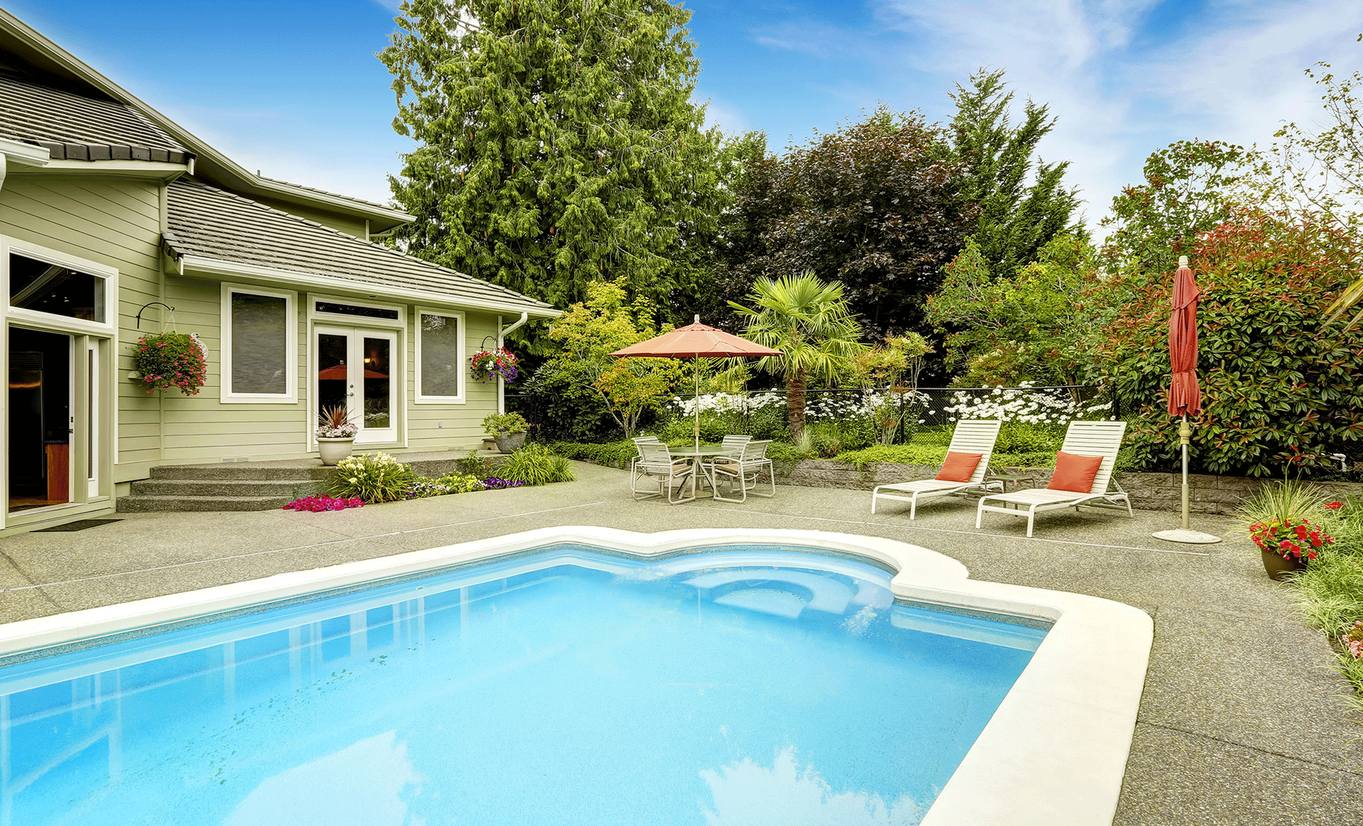 Backyard patio with a blue swimming pool, lounge chairs, and a house surrounded by greenery