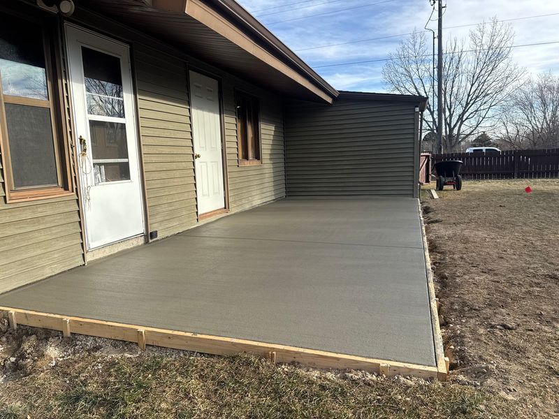 Concrete patio beside a beige house with white doors and a dark wood privacy wall