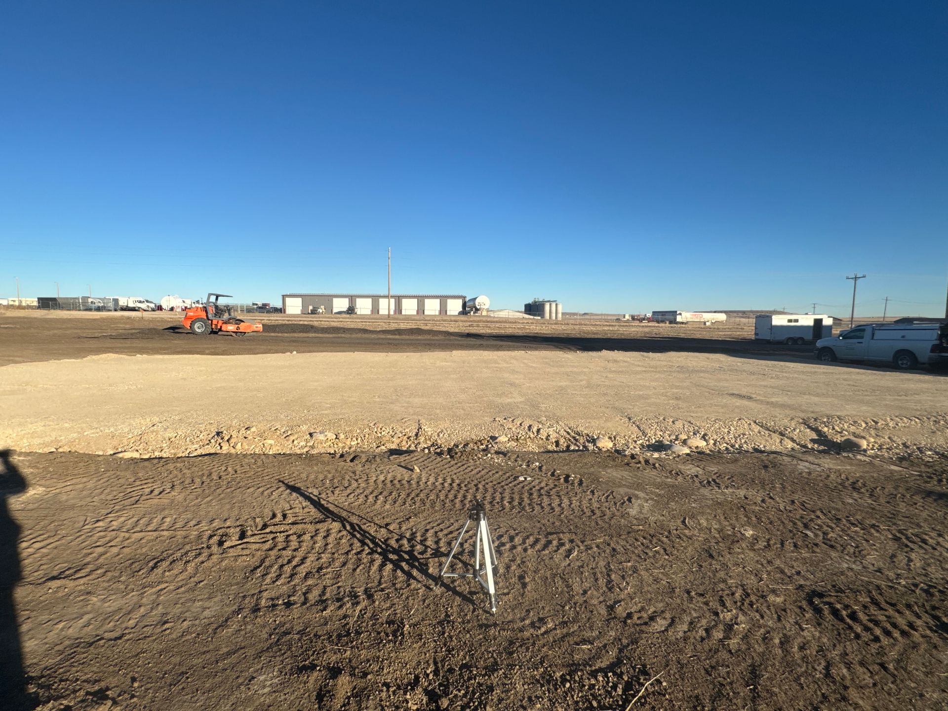 Empty dirt lot with a clear blue sky, construction equipment, and trailers in the distance
