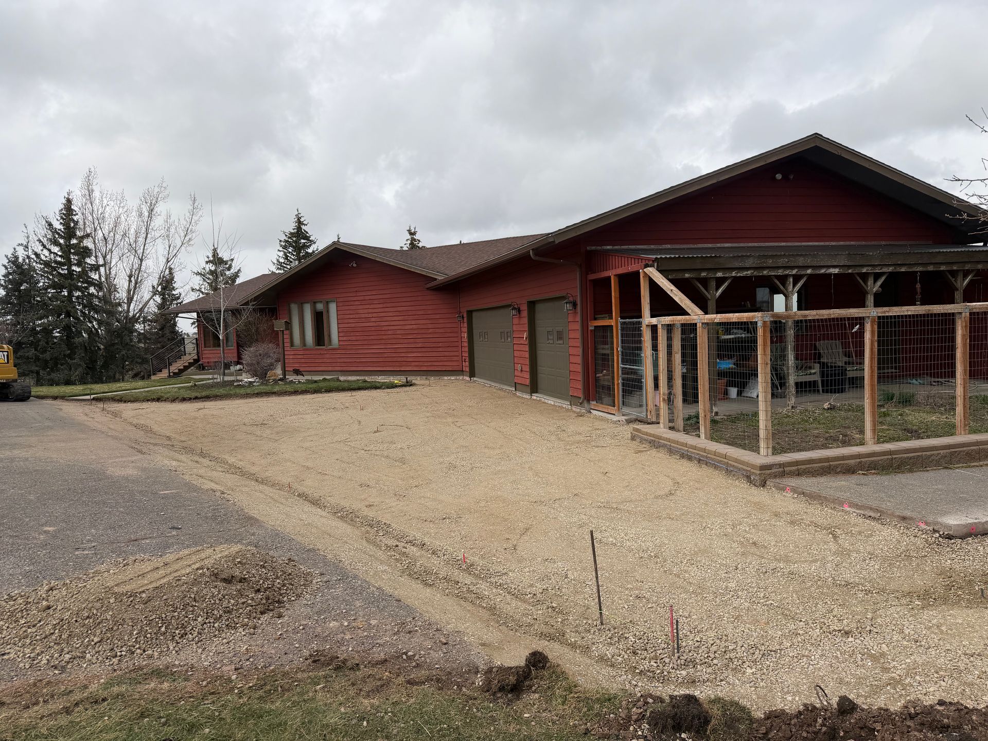 Red house with gravel driveway and a covered porch under a cloudy sky