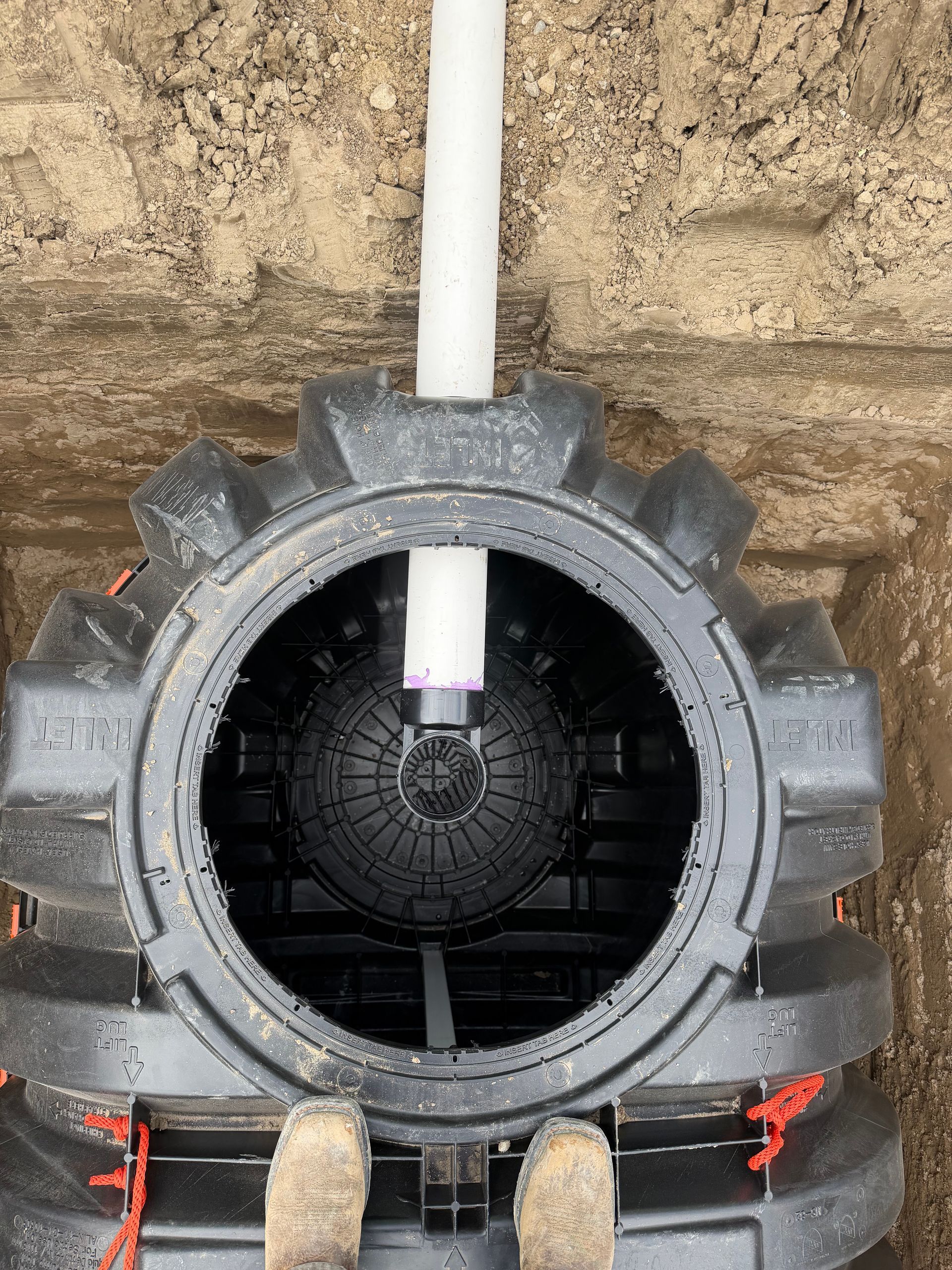 Large black tire-like tunnel opening against a stone wall, with a white pipe extending into the center.