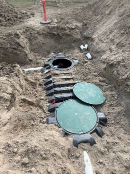 Trenched ground with septic tank access lids and exposed pipes during installation