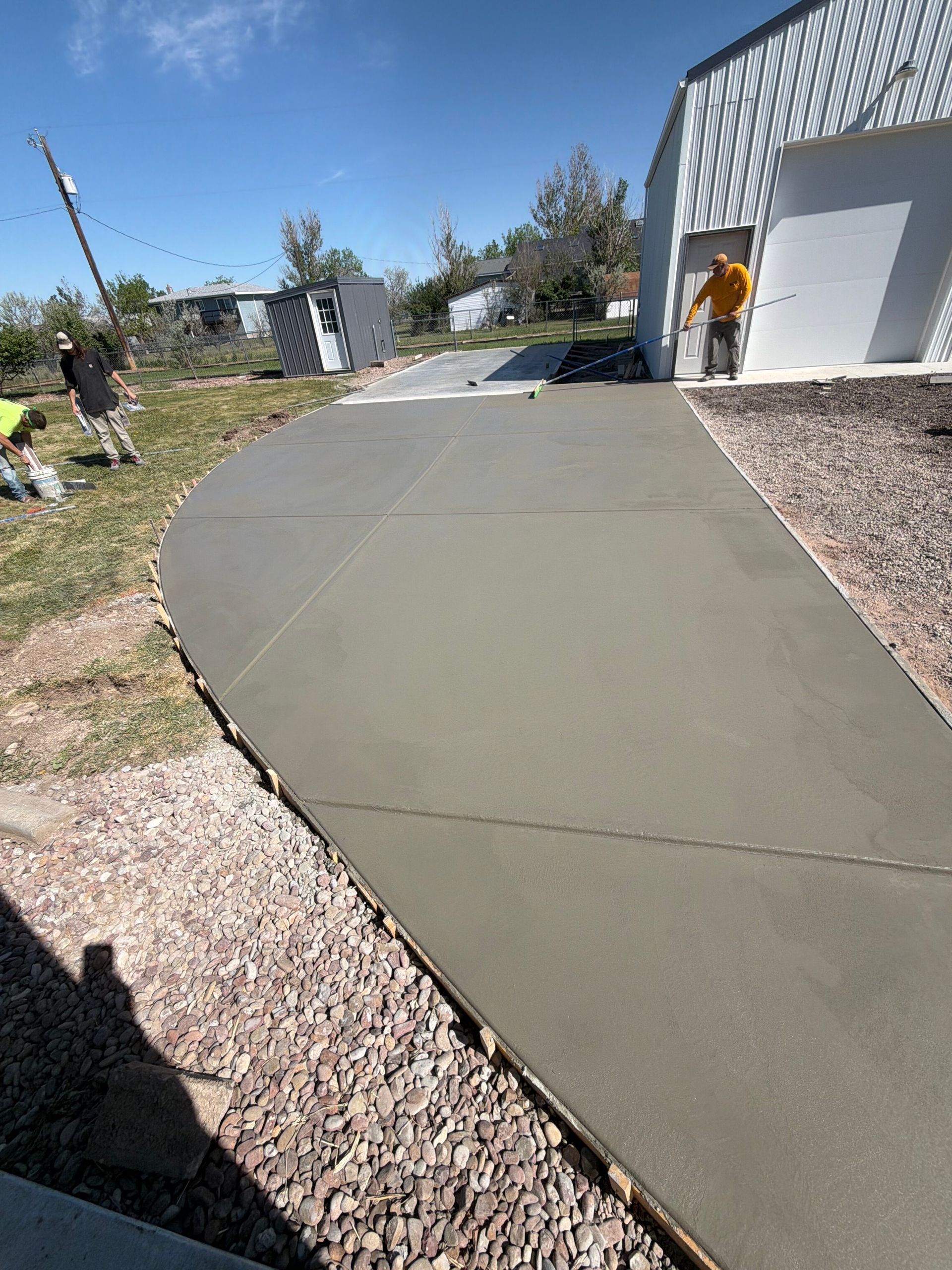 Concrete walkway beside a white building, with gravel landscaping and a person near the doorway.