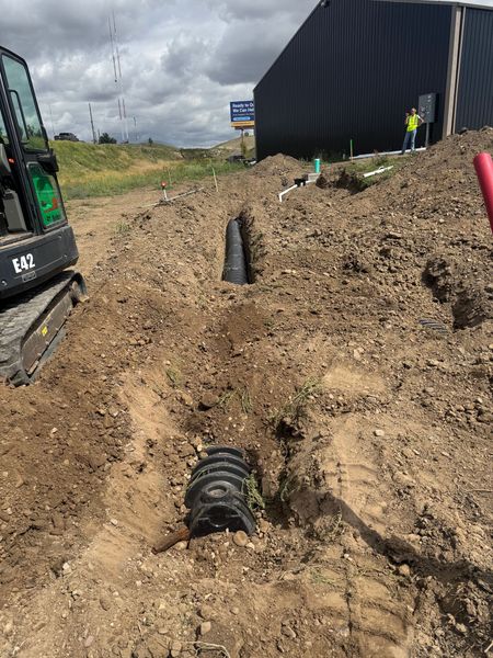 Construction trench with black drainage pipes beside a building and excavator tracks