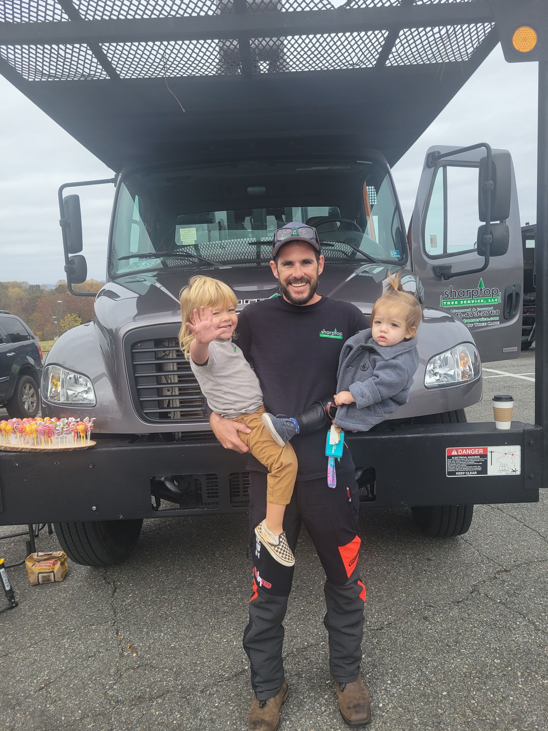 A man is holding two children in front of a truck.