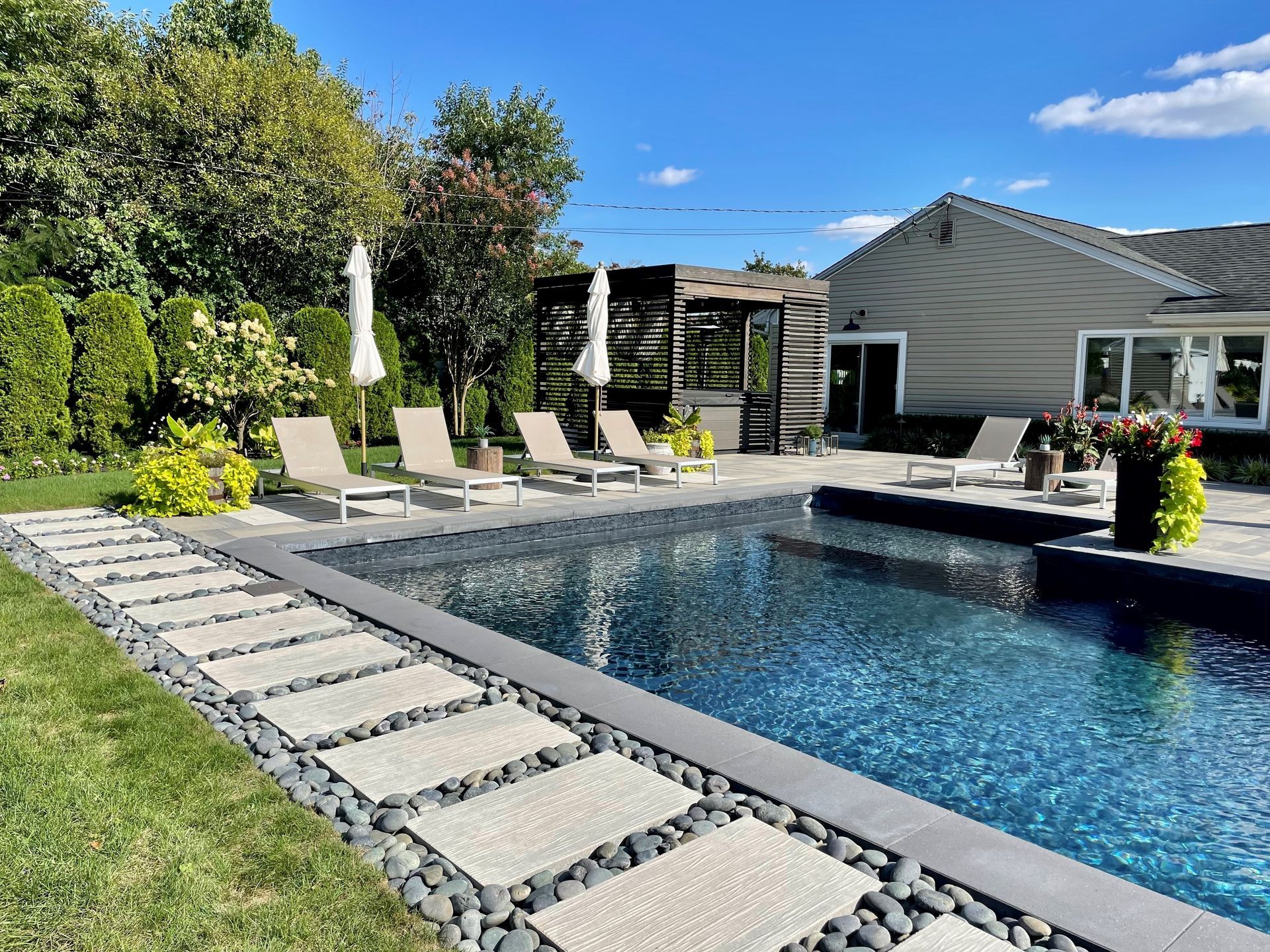 A large swimming pool with chairs and umbrellas in front of a house