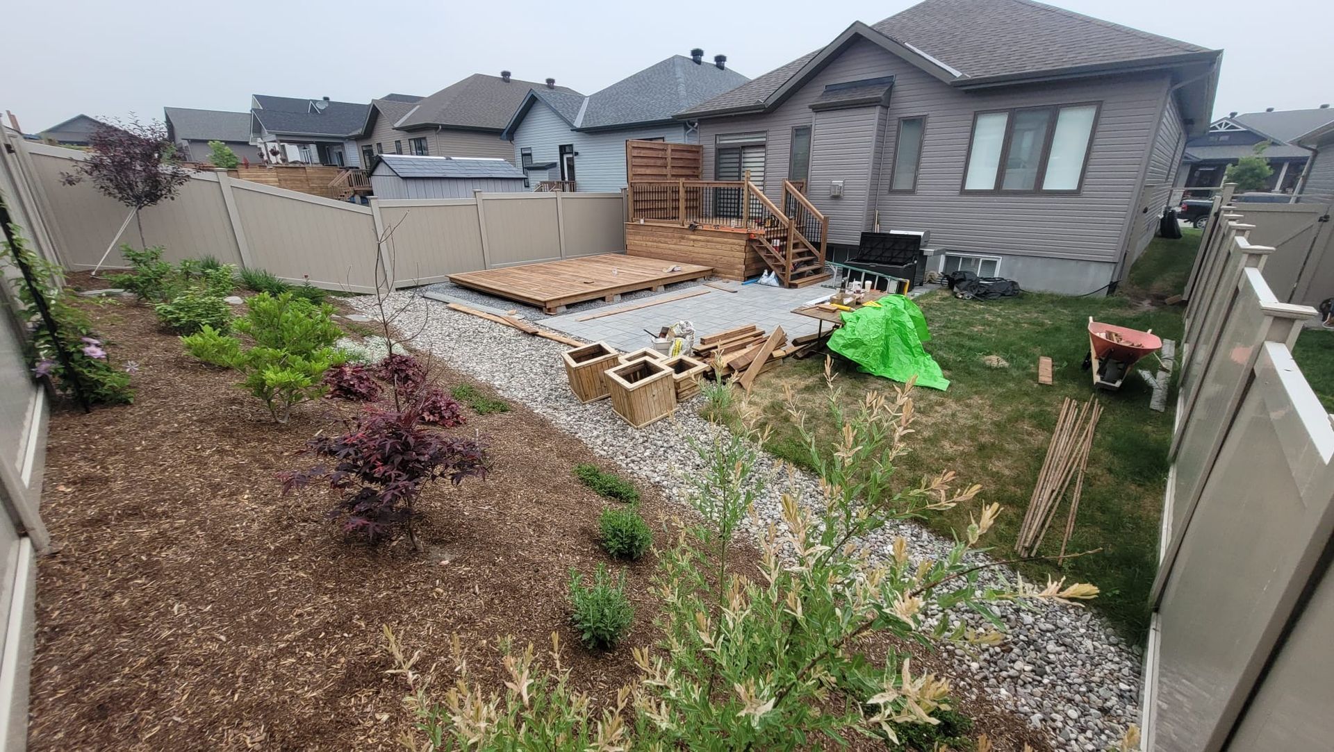 A brick pathway leads from a driveway to a house's front steps, beside a green lawn and bordering sidewalk. The pathway is bordered by a green lawn with a second house in the background.