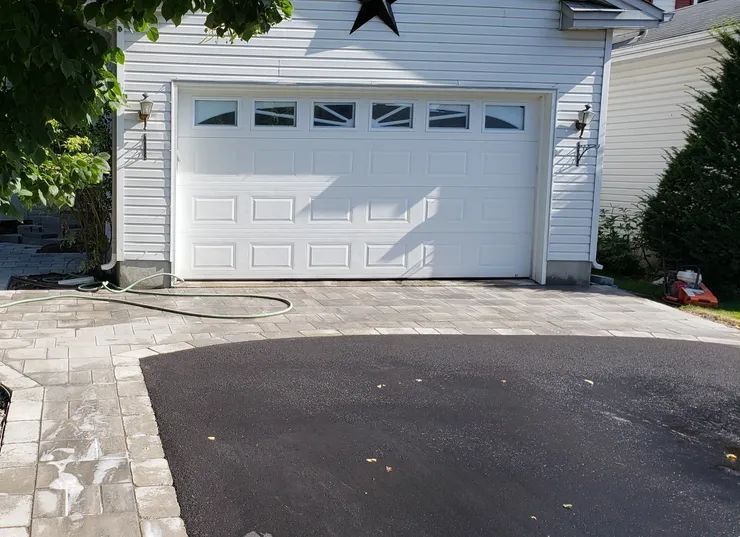 A white house with a white garage door and a black driveway.