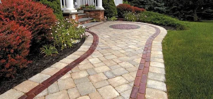 A brick walkway leading to a house in a lush green yard.