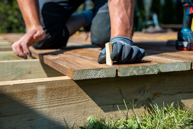 A man is kneeling down to build a wooden deck.