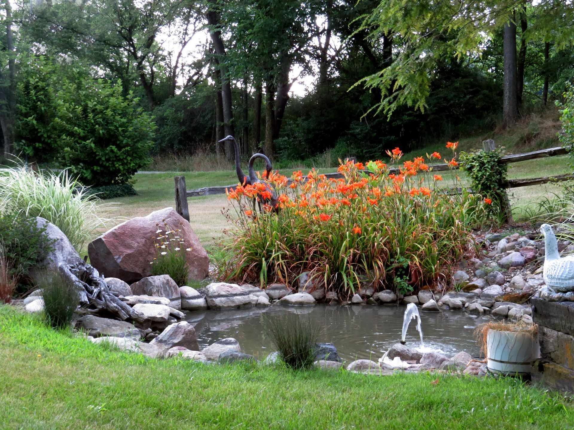 A pond surrounded by rocks and flowers with a fountain in the middle.