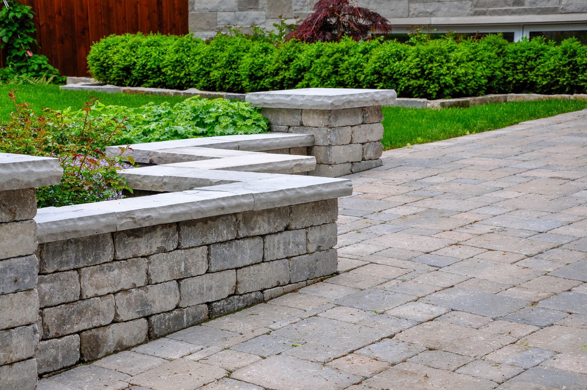 A brick walkway with a stone wall and benches in a garden.