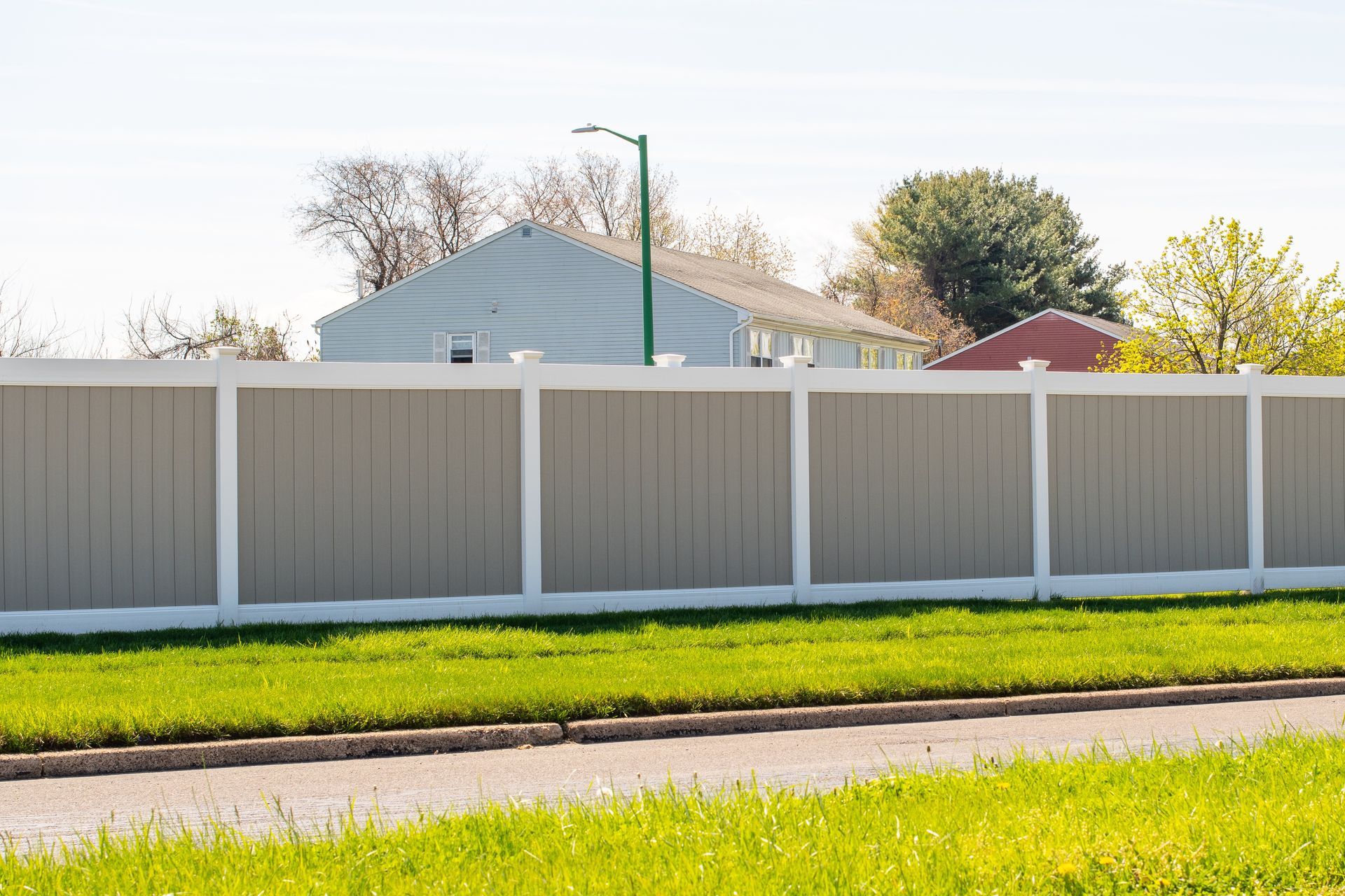 Gray and white privacy fence in front of a green lawn, with houses visible in the background on a sunny day.