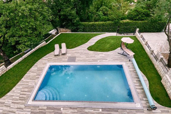 An aerial view of a large swimming pool in a backyard surrounded by trees.