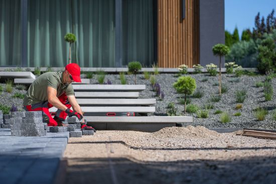 A man is laying bricks on the ground in front of a house.