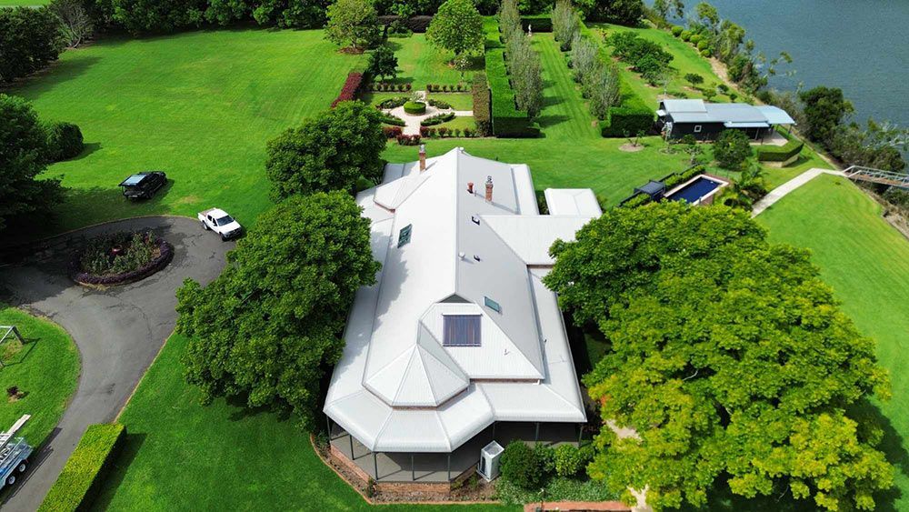An Aerial View of a Large House Surrounded by Trees and Grass — Tim Leach Metal Roofing in Wauchope, NSW