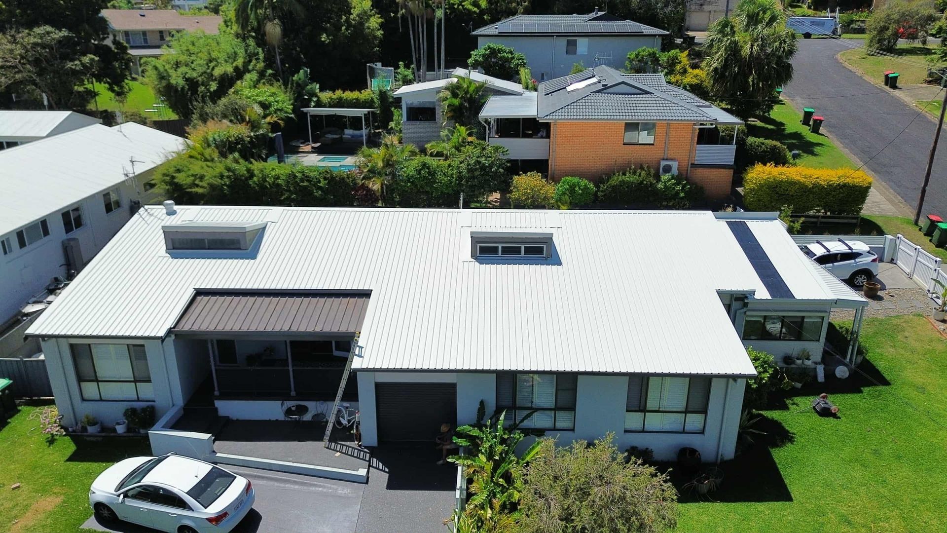 An Aerial View of a House With a White Metal Roof and Nearby Houses and Trees — Tim Leach Metal Roofing in Wauchope, NSW