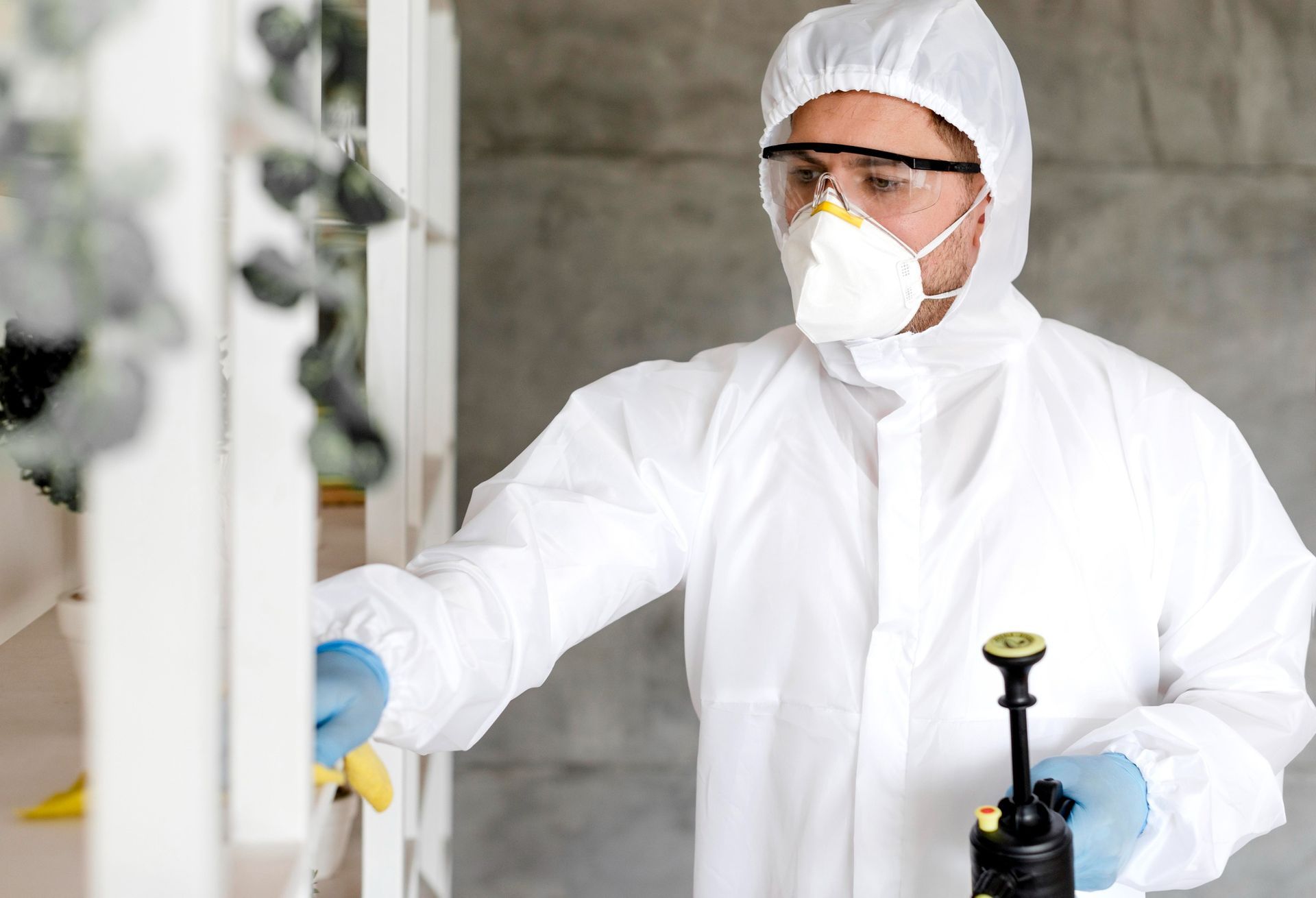 A man in a protective suit and mask is spraying a window.