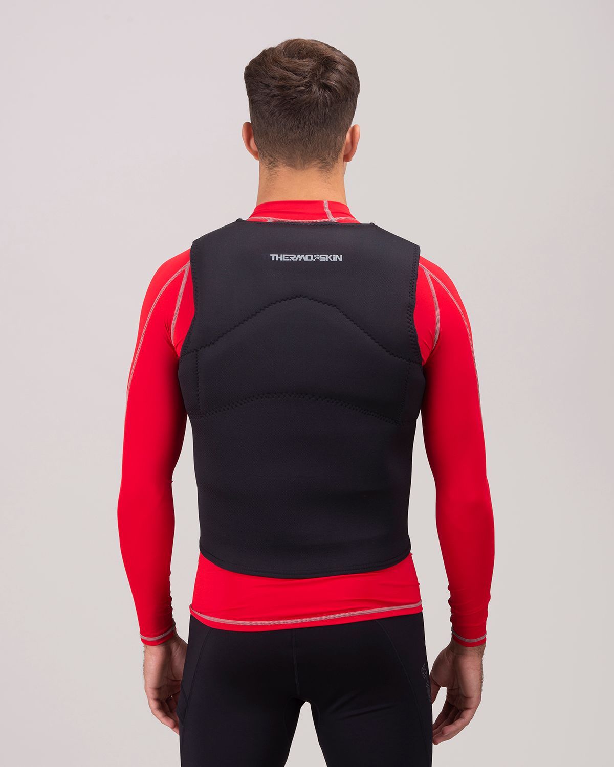 Hombre que lleva un chaleco antibalas negro para deportes acuáticos sobre una camisa roja de manga larga, vista trasera.
