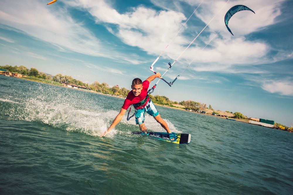 Hombre haciendo kitesurf en aguas azules bajo un cielo nublado, extendiendo una mano.