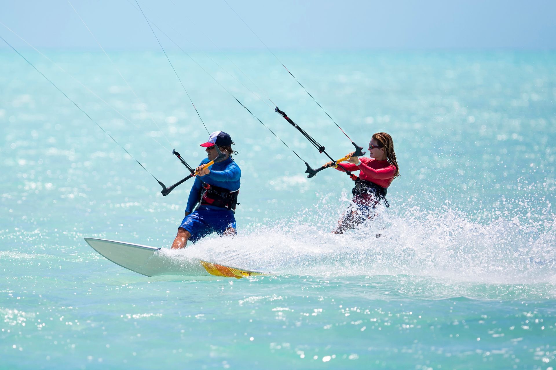 Hombre haciendo kitesurf en aguas azules bajo un cielo nublado, extendiendo una mano.