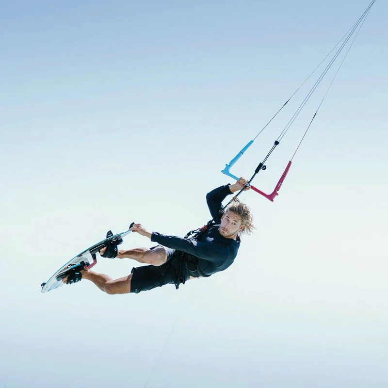 Persona sosteniendo una barra de kitesurf con mangos rosas y azules contra un cielo brillante.