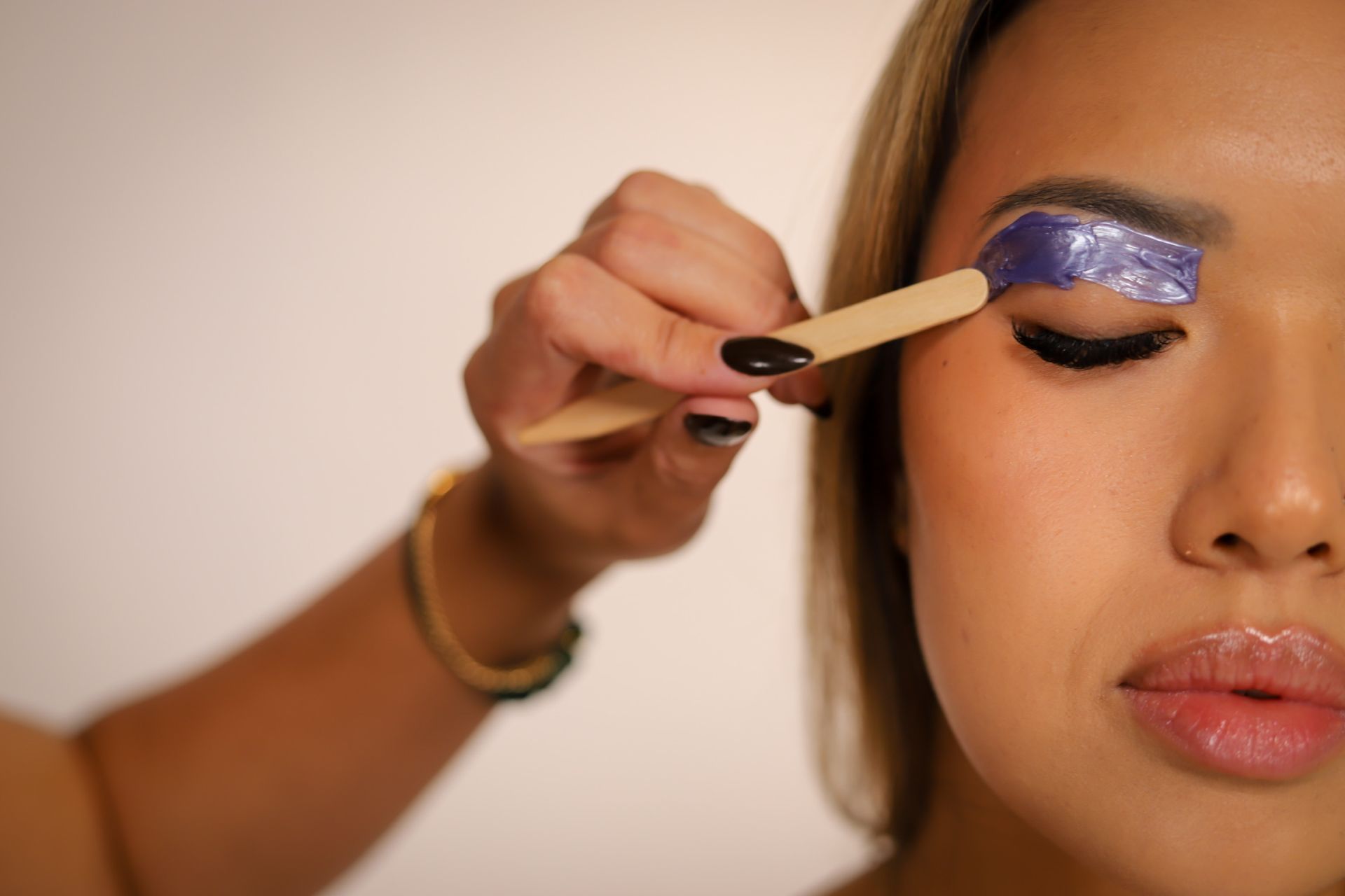 Makeup artist applying glittery purple eyeshadow to a woman’s closed eyelid