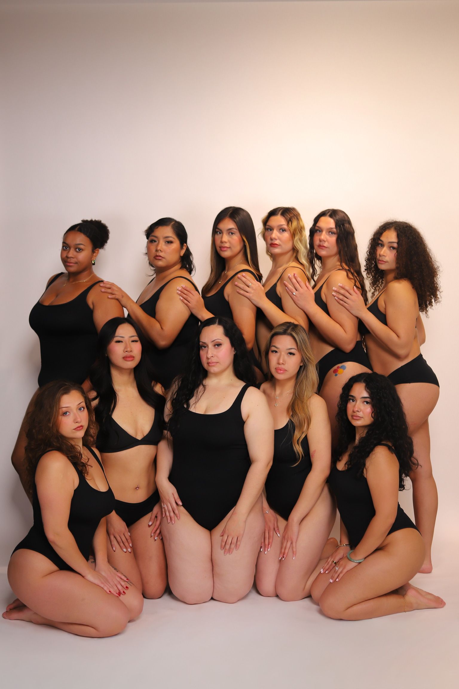 Eleven women in black swimsuits pose together in front of a white backdrop.