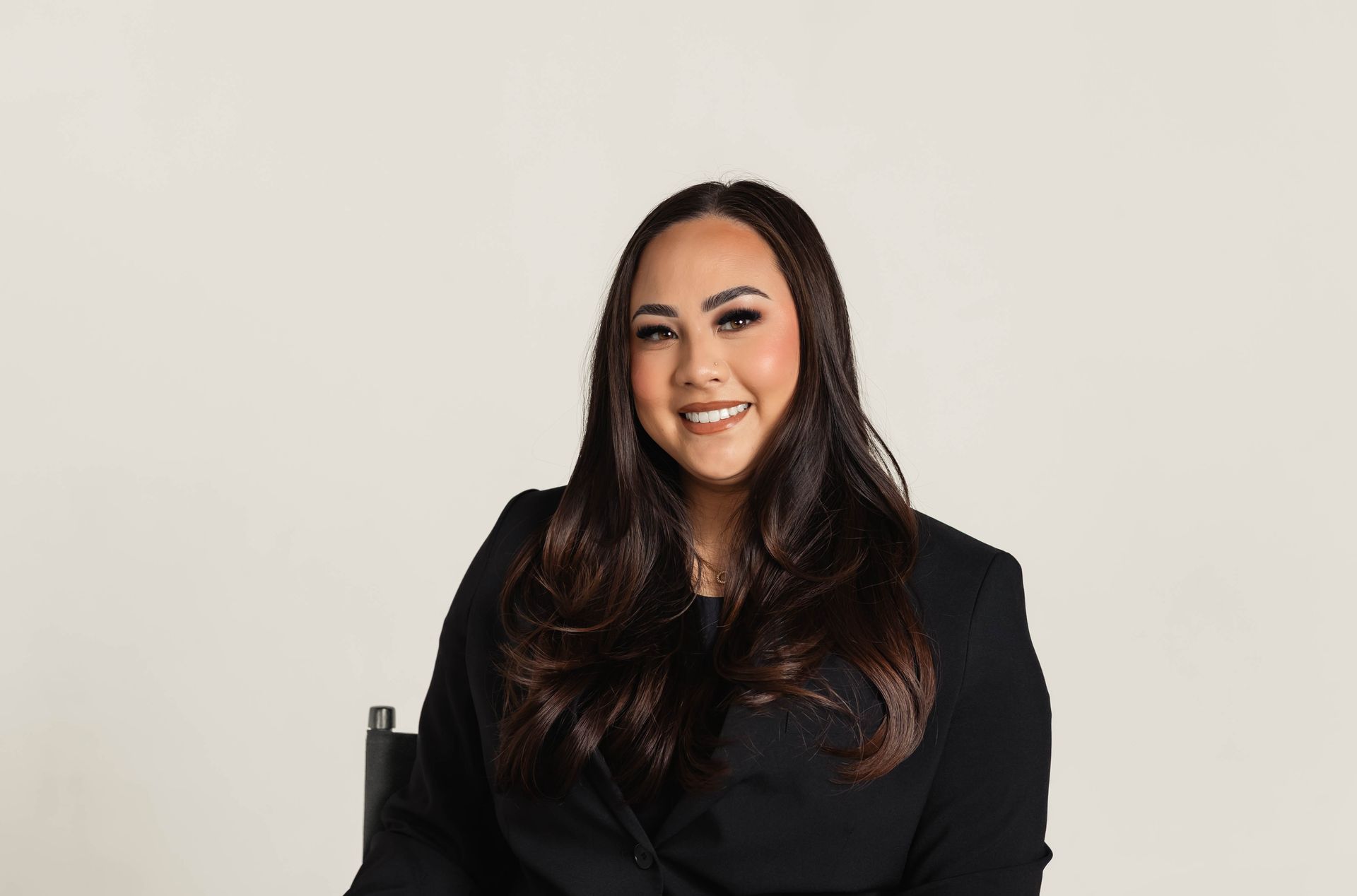 Smiling person with long dark hair in a black blazer against a light background