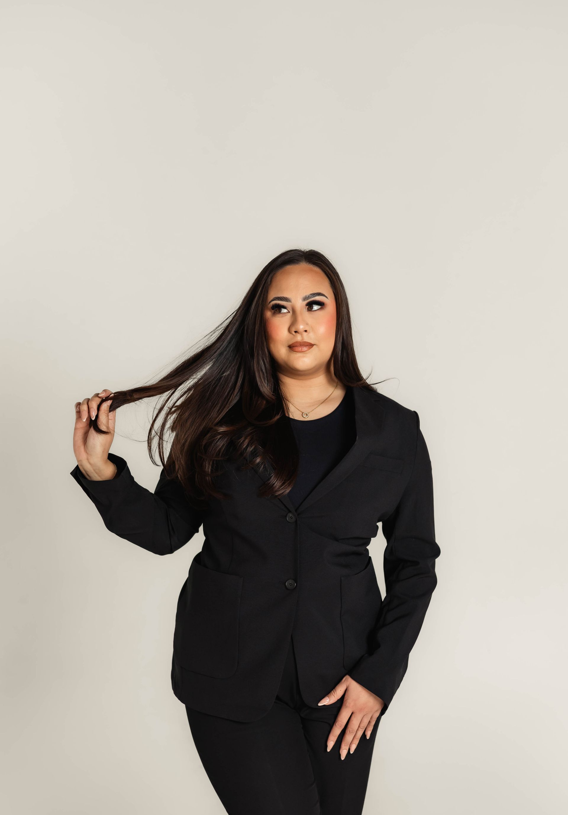 Woman in black dress and heels, poses on white background.