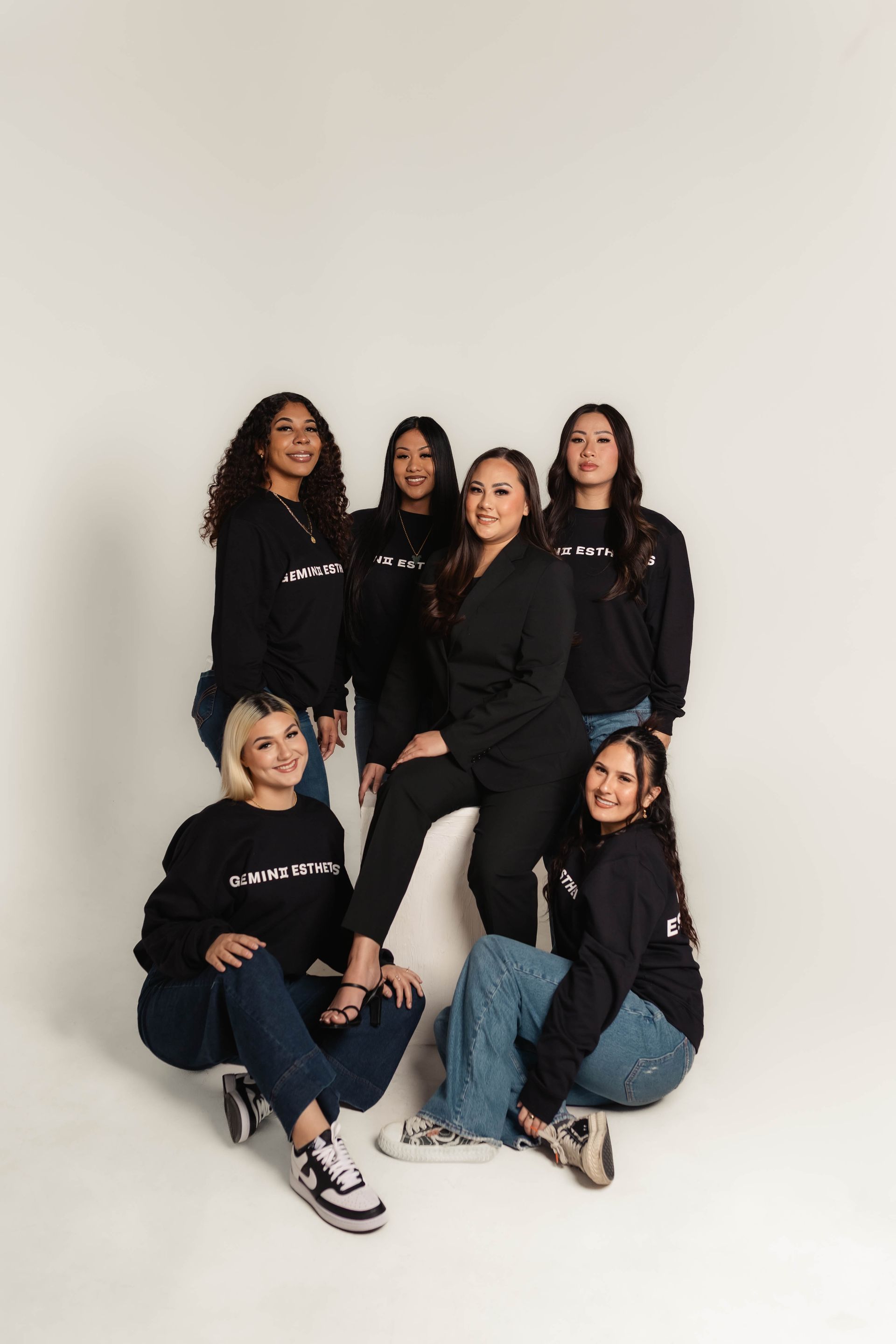 Six people posing in black outfits against a plain white backdrop