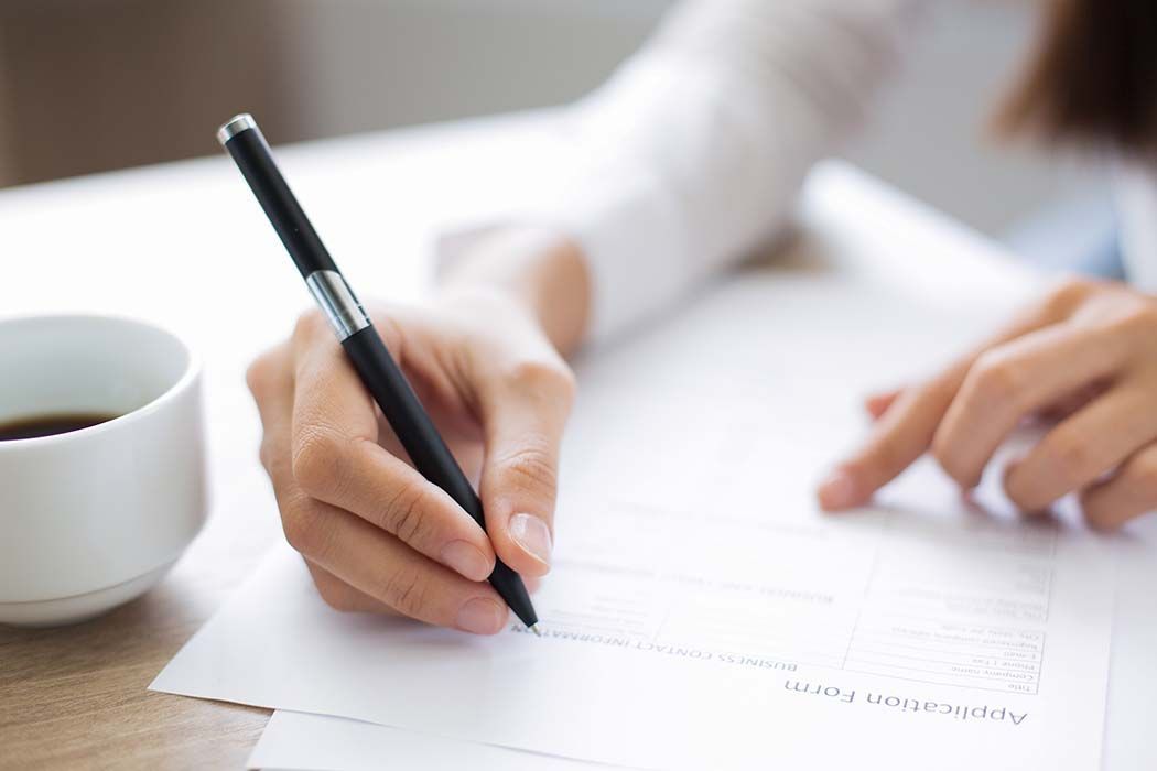 A person writing on a paper with a pen, next to a coffee cup.
