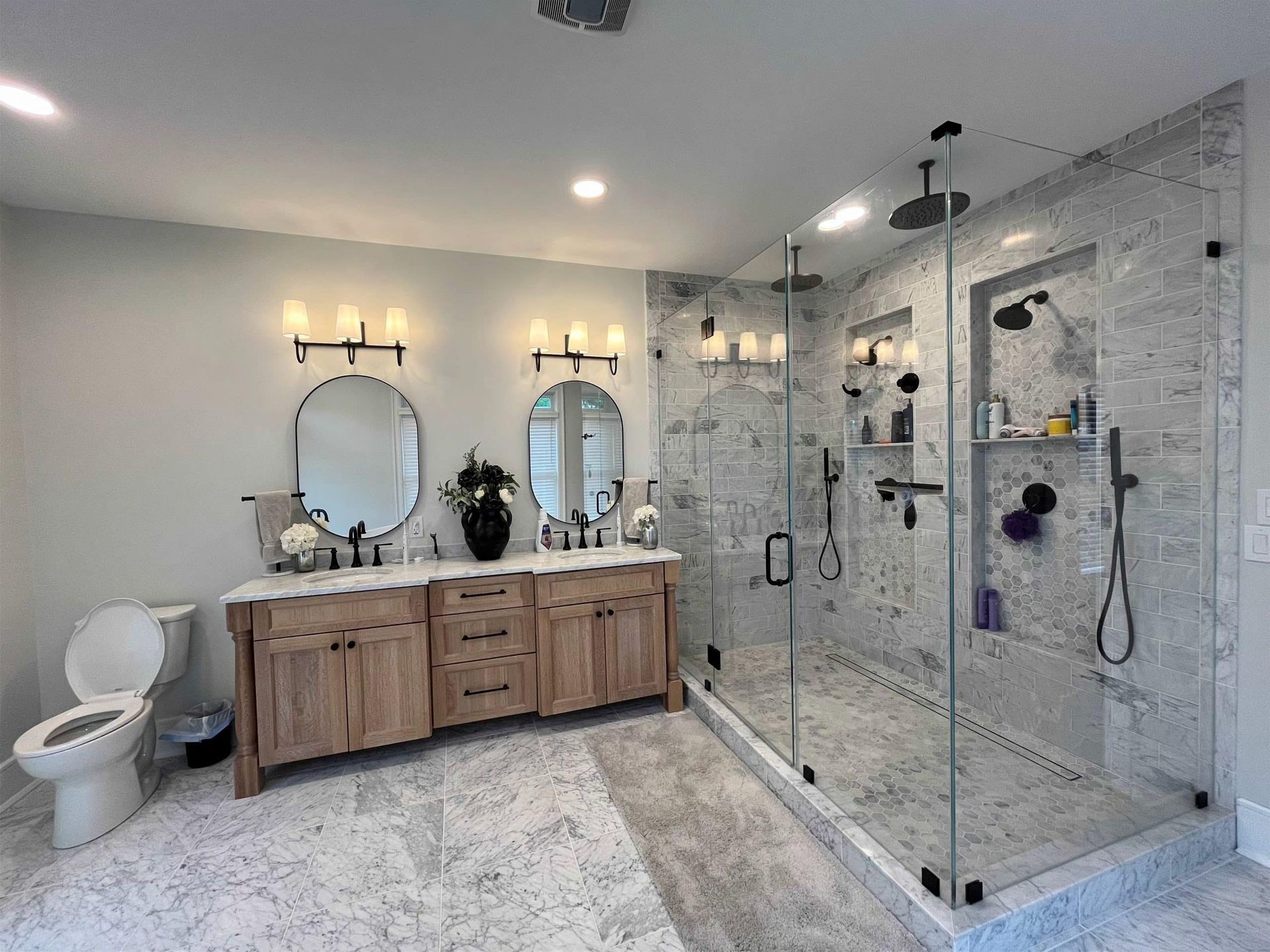 Modern bathroom with double vanity, round mirrors, toilet, and glass-enclosed shower on white tile floor