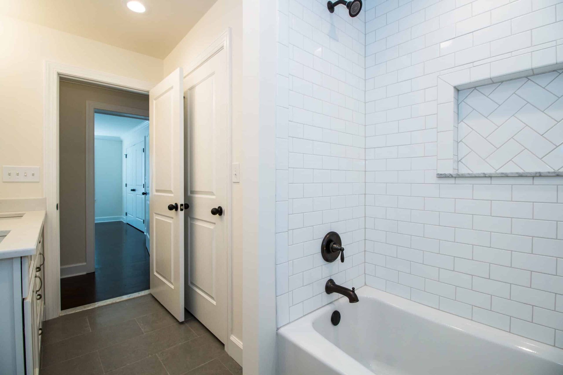 Bright bathroom with white subway tile, tub, and open door to a hallway