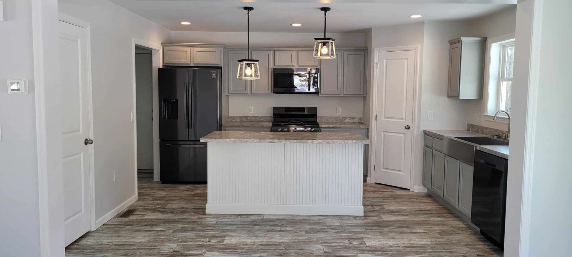 Bright modern kitchen with gray cabinets, white island, pendant lights, and stainless steel appliances