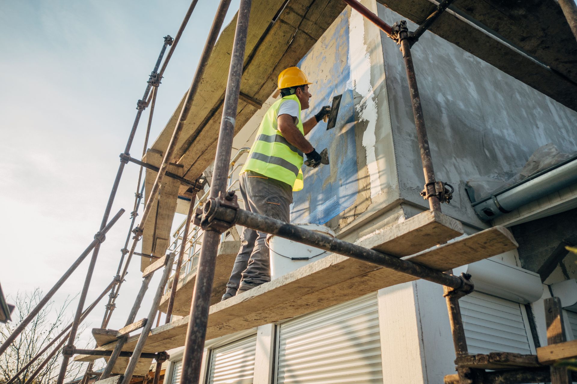 Construction worker applying plaster to building exterior from scaffolding.