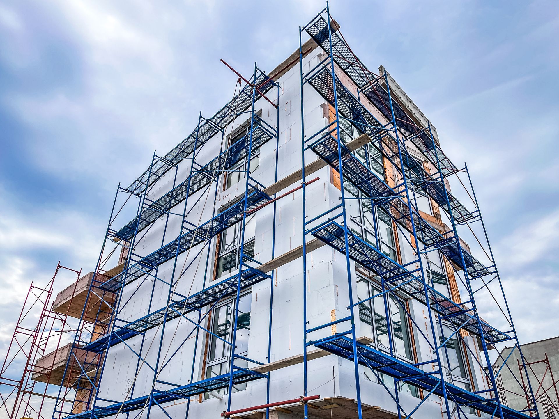 Building under construction with blue scaffolding against a cloudy sky.