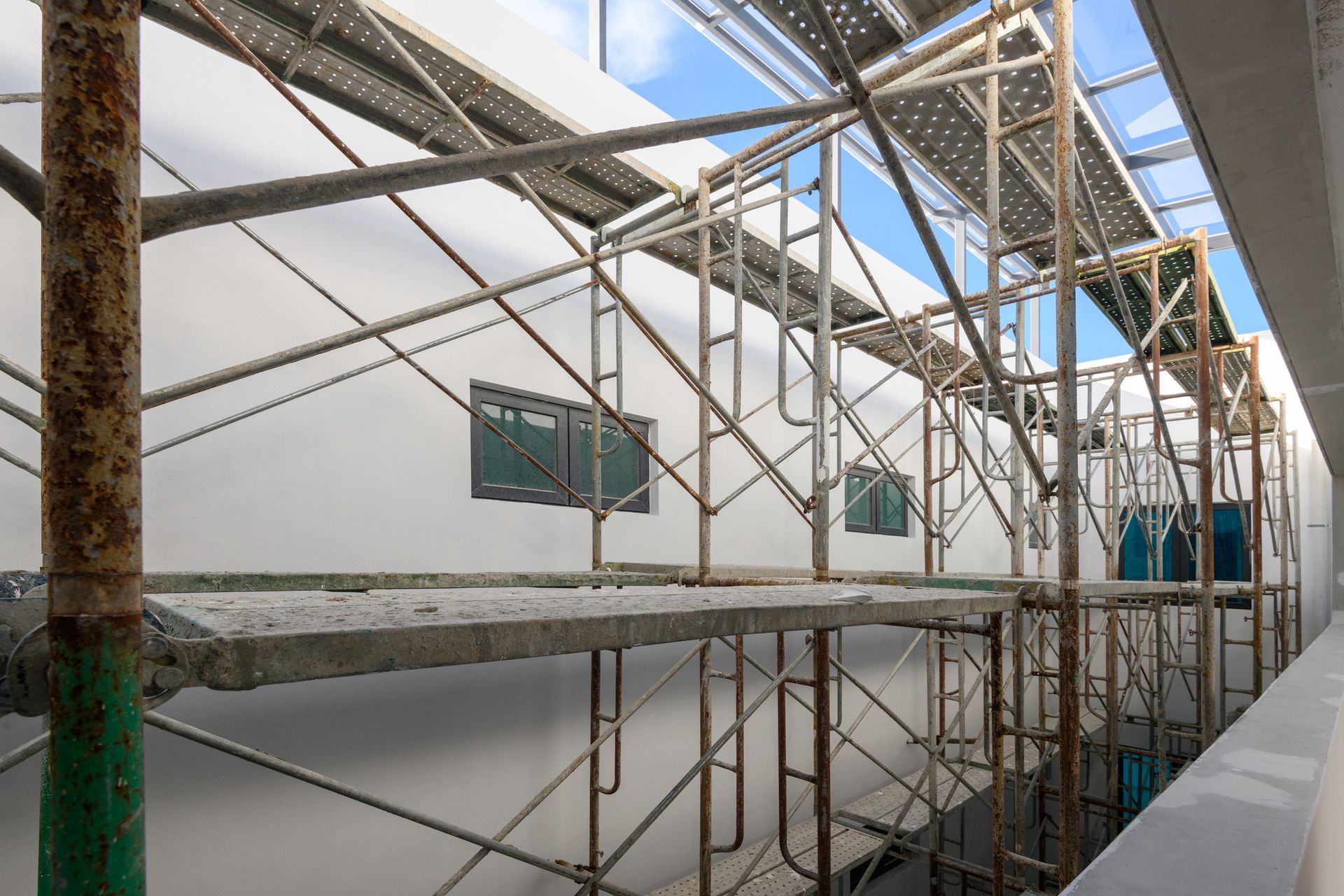 Scaffolding along a white building wall with a partial view of the sky.