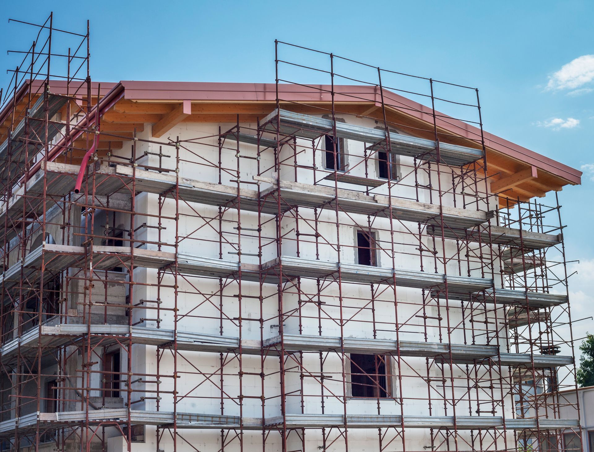 Building under construction with scaffolding; white walls, wooden roof, blue sky.