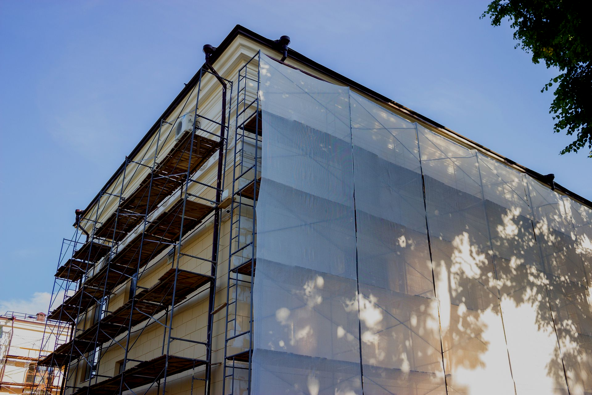 Building facade covered in white protective netting and scaffolding. Sunny outdoor setting.