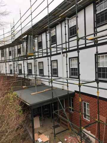 Scaffolding surrounds a multi-story building with white walls, black trim, and red brick.