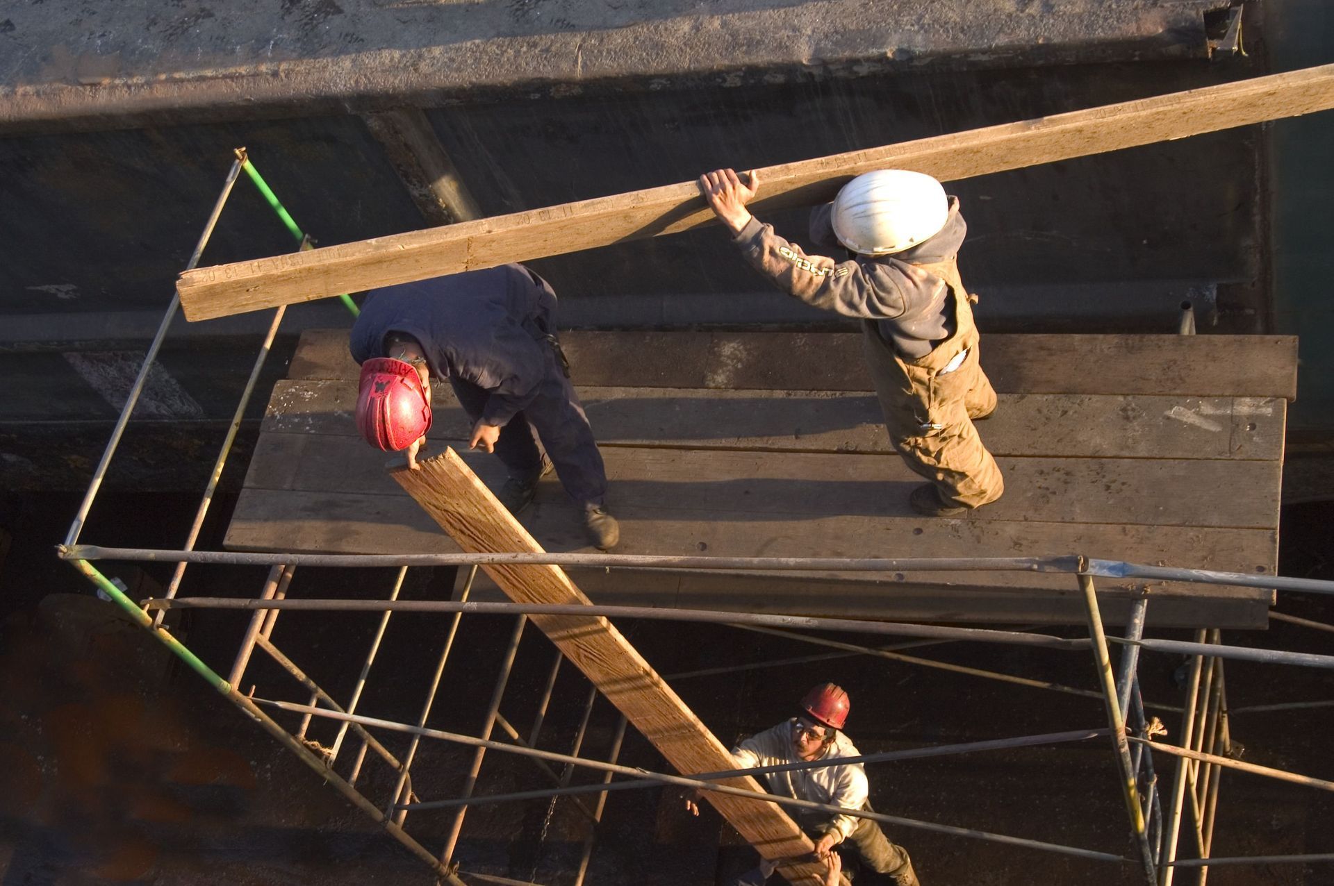 Three construction workers on scaffolding, carrying wooden beams.